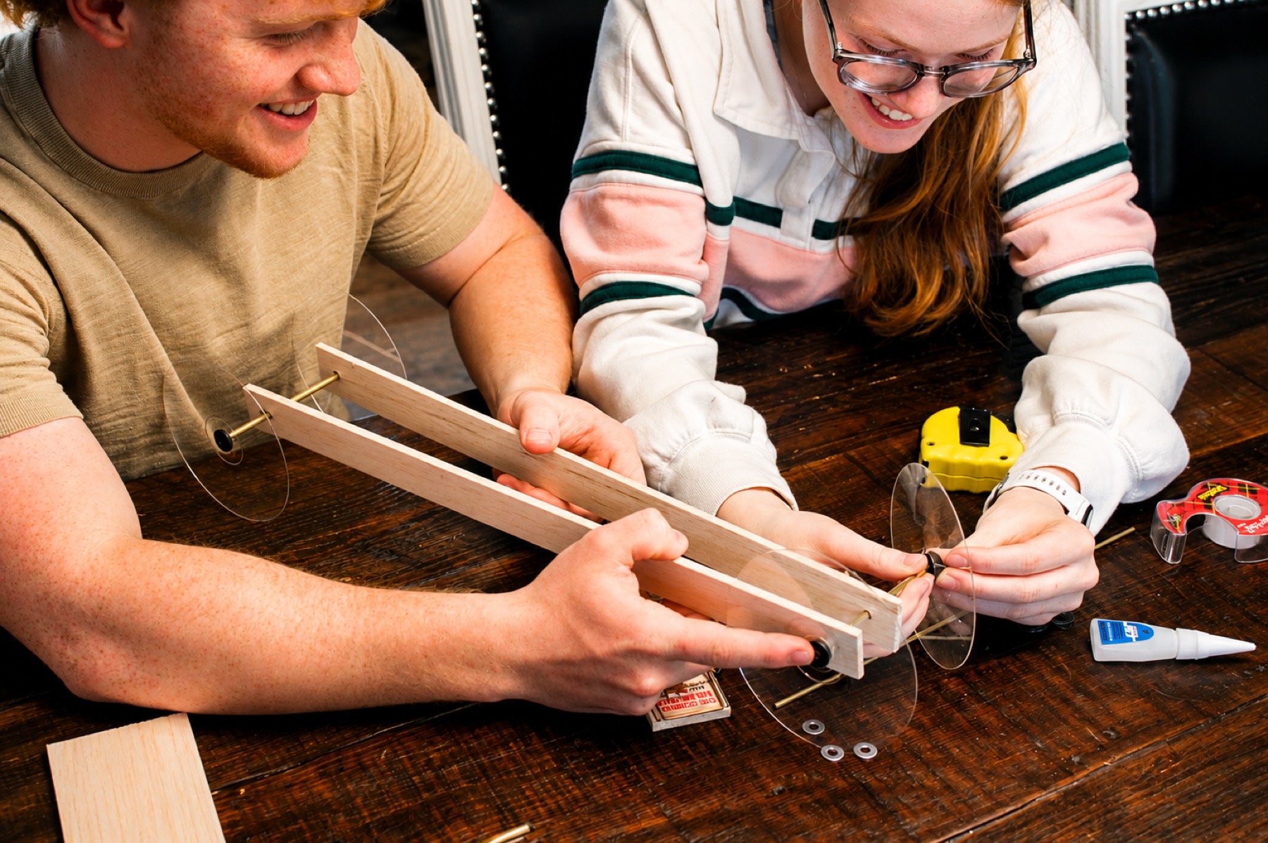 Mid-build at a kitchen or co-op table, the chassis taking shape, tape measure and glue in frame.