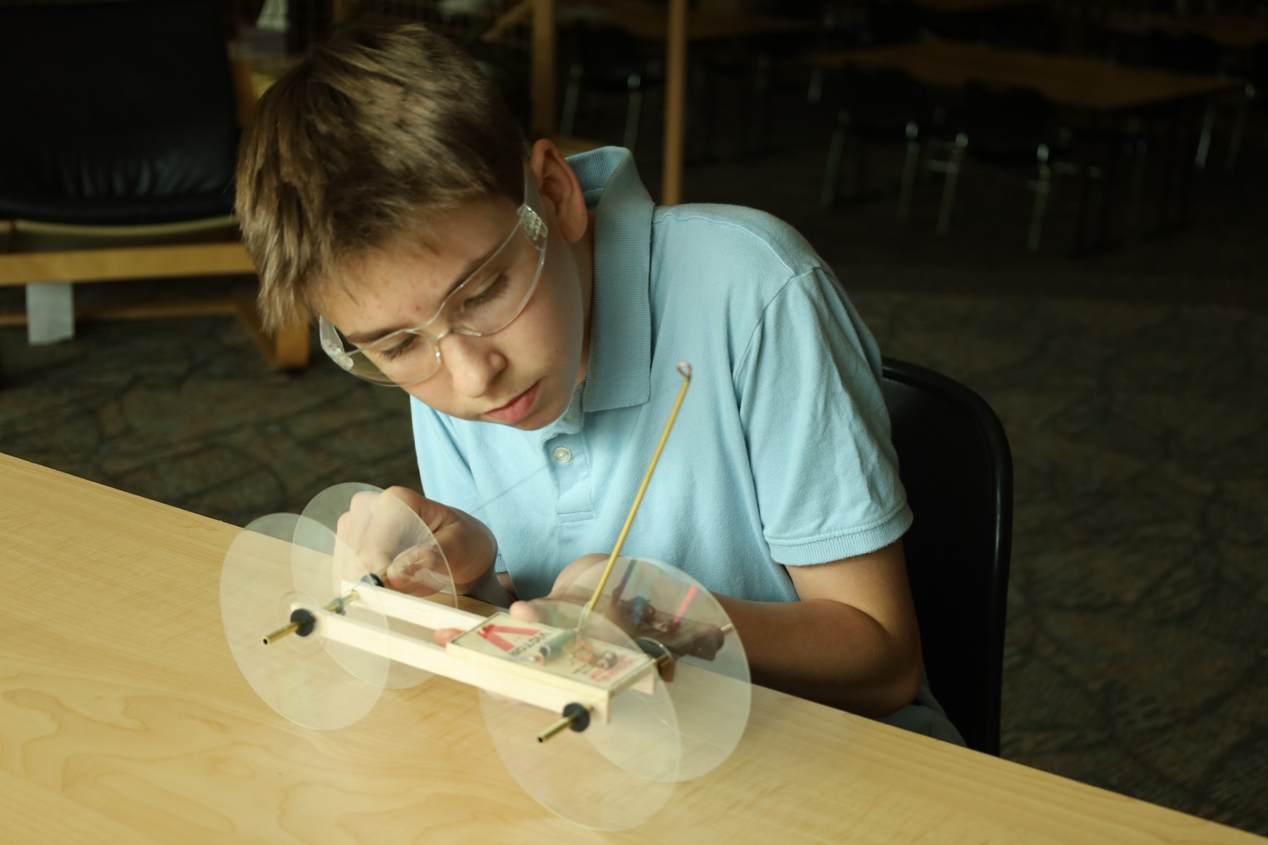 Student in safety glasses fine-tuning the mousetrap car at the build table.