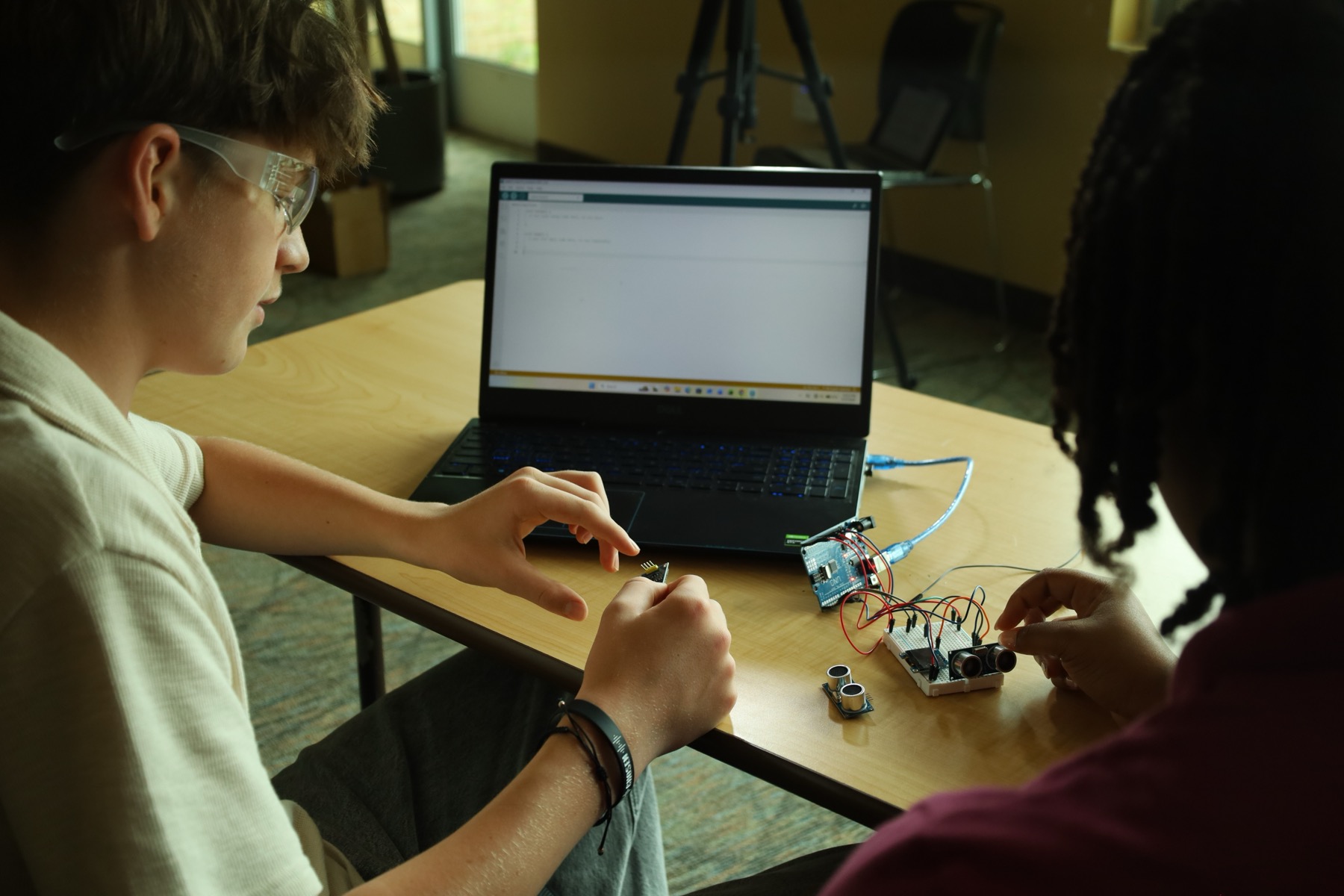 Two students wiring the Arduino distance sensor, the lesson open on the laptop.